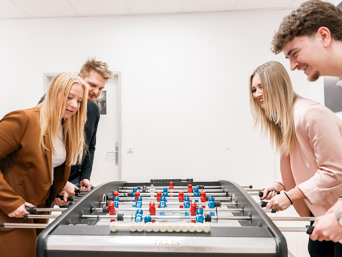 Zwei Mitarbeiterinnen und zwei Mitarbeiter spielen Tischfußball im Büro bei fidas Innsbruck