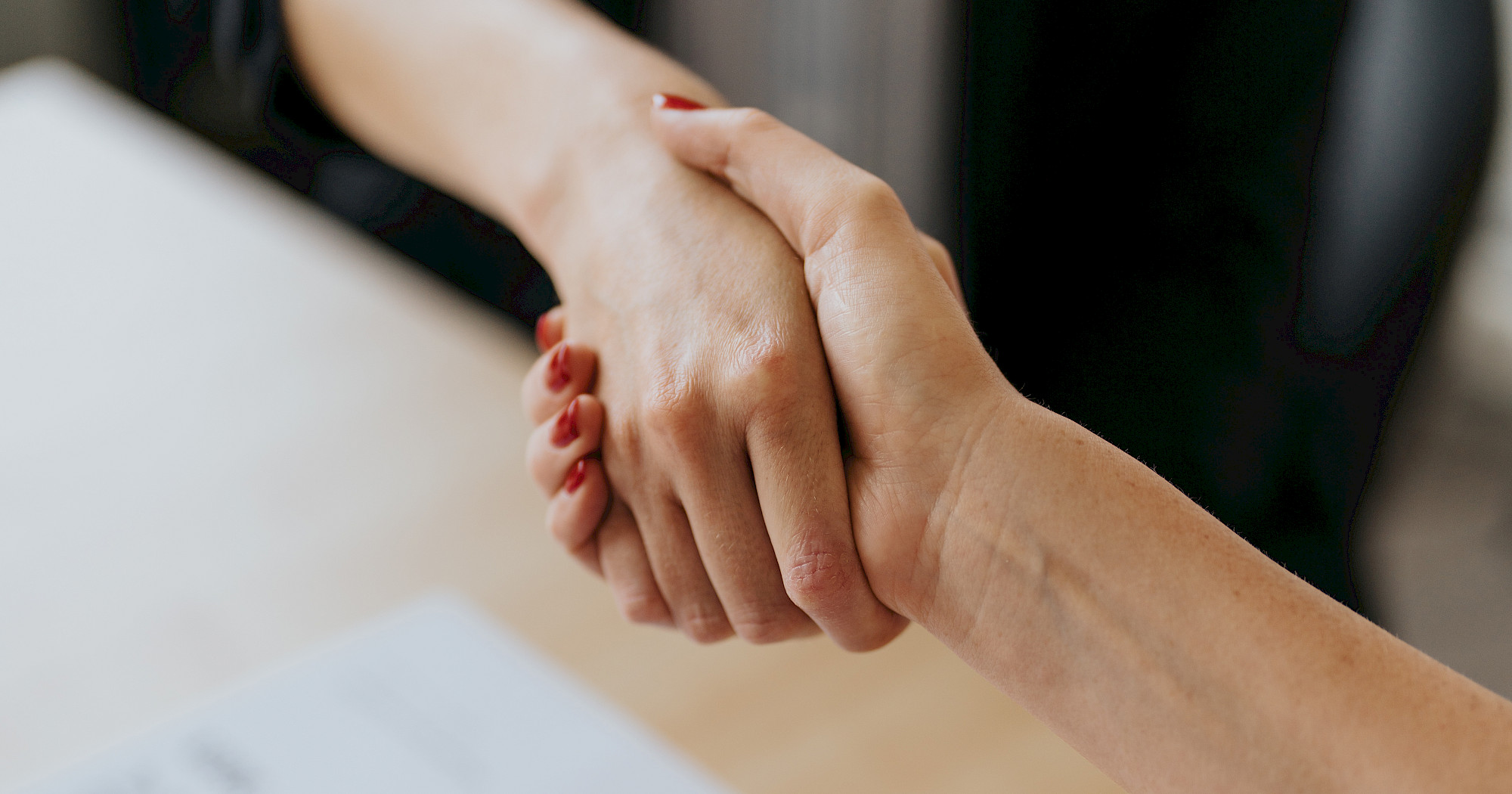 Zwei Personen geben sich bei einem Beratungsgespräch zur Auftraggeberhaftung die Hand, auf dem Tisch liegen Fidas-Unterlagen.