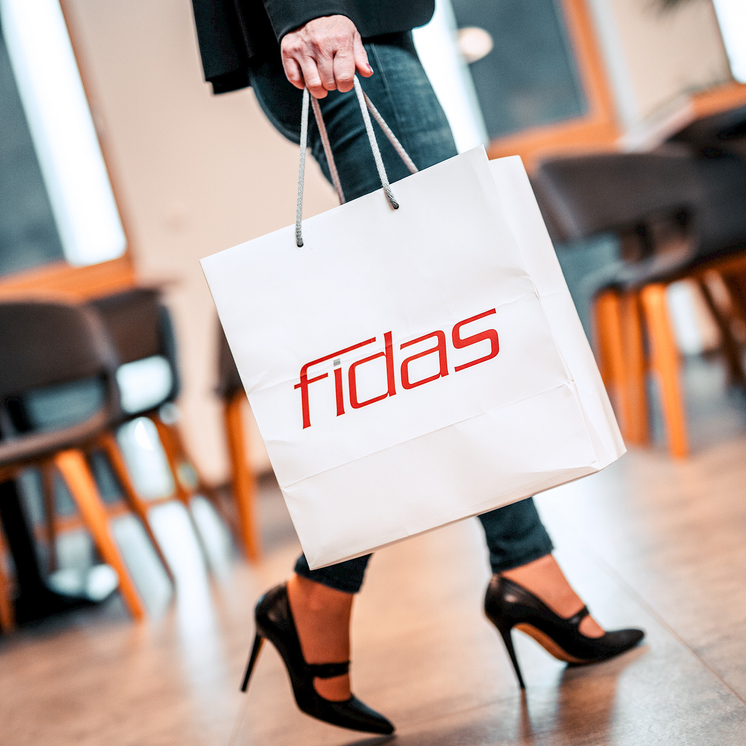 Frau in Stöckelschuhen geht mit einer Fidas-Einkaufstasche durch Bürogebäude.