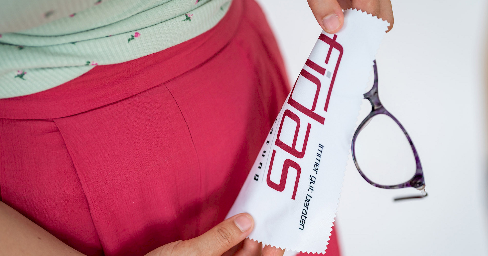 Frau hält ein Brillentuch mit Fidas Steuerberatung Logo und ihre Brille in den Händen.