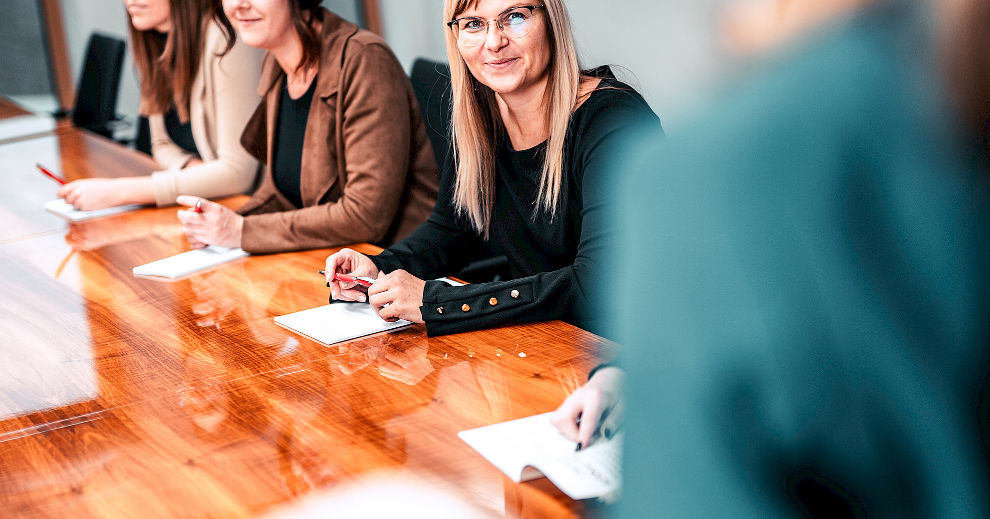 Führungsperson präsentiert vor der Belegschaft an einem langen Meetingtisch.